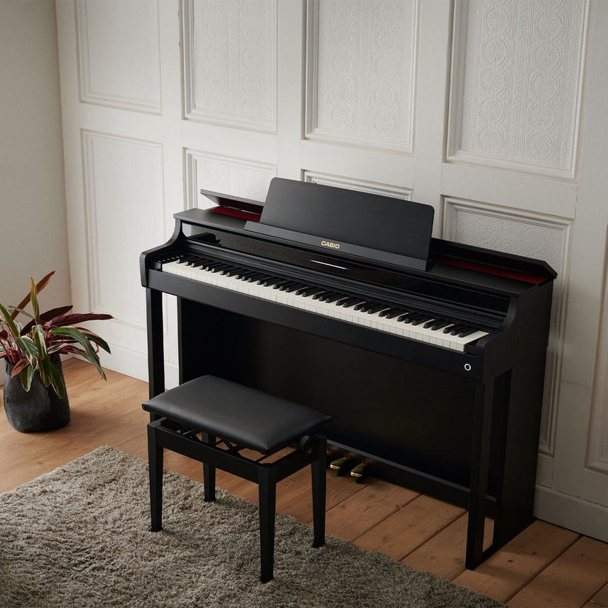 Piano numérique Casio AP-550BK noir – vue de trois quarts dans un salon avec banquette noire.