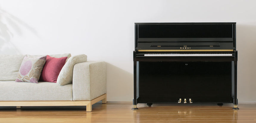 Piano droit Kawai K-300 noir brillant – vue de face à côté d’un canapé.